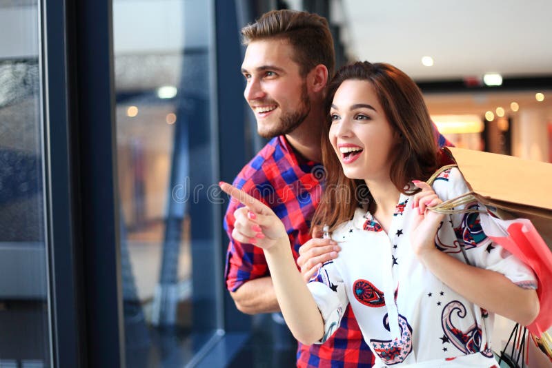 Vendita, consumismo e concetto della gente - giovane coppia felice con i sacchetti della spesa che camminano nel centro commercia