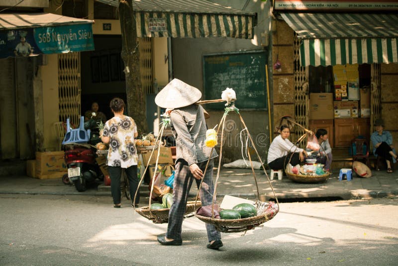 Hanoi, Vietnam - 26 April, 2014: Woman vendor carrying baskets with fruits on the street of Hanoi on 26 April 2014, Vietnam. Hanoi, Vietnam - 26 April, 2014: Woman vendor carrying baskets with fruits on the street of Hanoi on 26 April 2014, Vietnam.