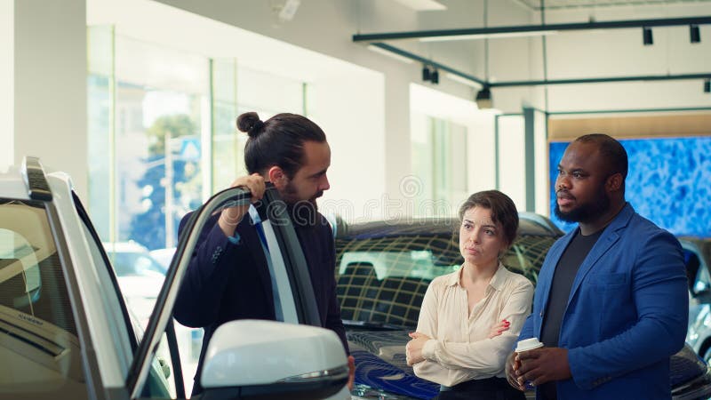 Venditore di concessionari che apre la porta dell'auto spiegando vari aspetti dell'autoveicolo fotografia stock