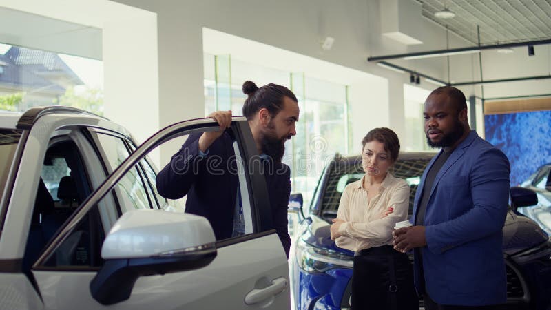 Venditore di concessionari che apre la porta dell'auto spiegando vari aspetti dell'autoveicolo fotografia stock libera da diritti