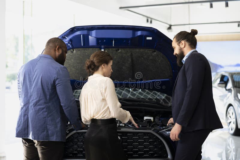 Venditore di concessionari che mostra i componenti dei clienti sotto cappuccio. Venditore di concessionari che fornisce ai clienti una conoscenza approfondita delle caratteristiche del veicolo, mostrando componenti di qualità sotto cappuccio. showroom agent parla con i clienti della potenza del motore all'interno dell'auto