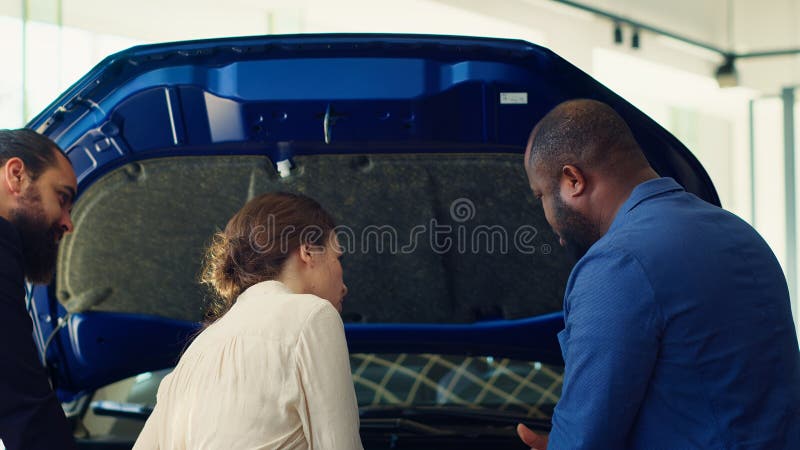 Venditore di concessionari che risponde ai clienti domande sulle auto che mostrano i componenti usati fotografia stock