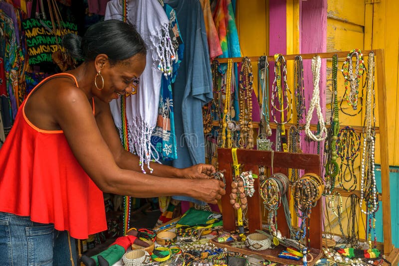 Montego Bay, Jamaica - June 04 2015: Smiling Jamaican female vendor selling bead chains and other hand made craft items, jewellery and clothes a craft market in Montego Bay, Jamaica. Montego Bay, Jamaica - June 04 2015: Smiling Jamaican female vendor selling bead chains and other hand made craft items, jewellery and clothes a craft market in Montego Bay, Jamaica.