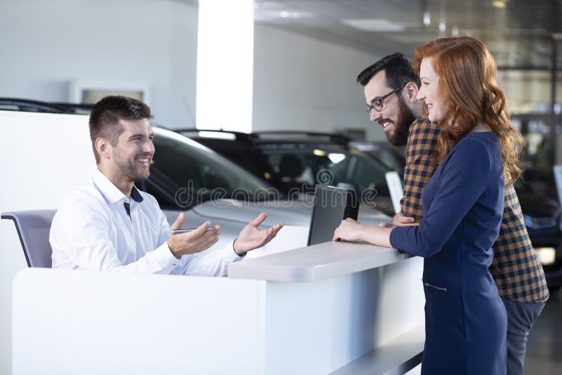 Venditore sorridente dell'automobile che parla con i compratori felici in sala d'esposizione esclusiva