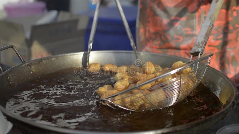 Vendor is picking many deep fried flour in a pan. Deep fried dough stick in bubbling oil.