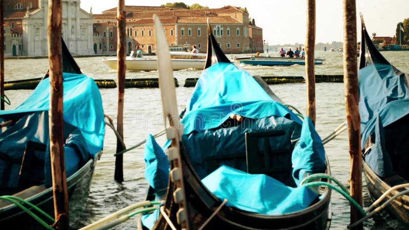 VENEZIA, ITALIA - 8 AGOSTO 2017 Gondole veneziane attraccate che ondeggiano contro il paesaggio urbano ed i motoscafi commoventi fotografia stock VENEZIA, ITALIA - 8 AGOSTO 2017 Gondole veneziane attraccate che ondeggiano contro il paesaggio urbano ed i motoscafi commoventi fotografia stock