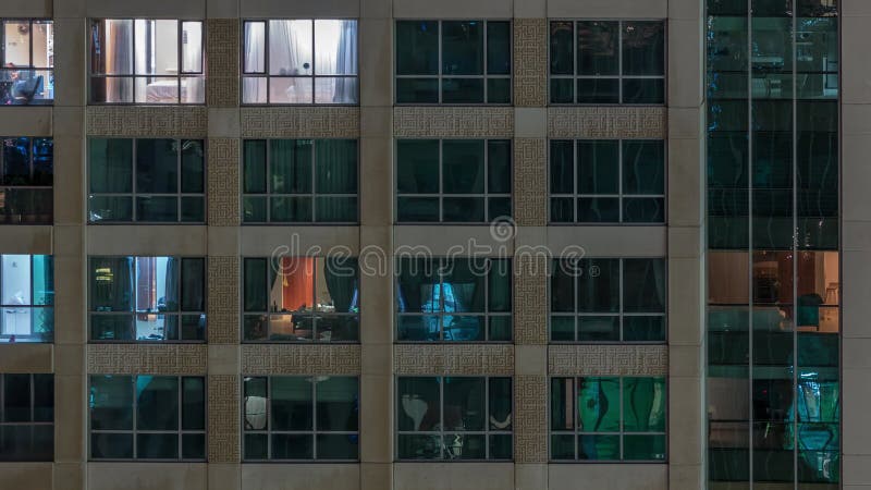 Ventanas del edificio de varias plantas con iluminación interior y personas en movimiento en los apartamentos, lapso de tiempo