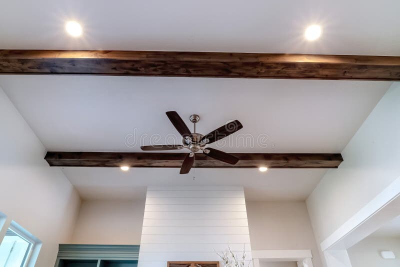 Ventilador de techo con luces entre vigas de madera decorativas dentro de sala de estar de casa