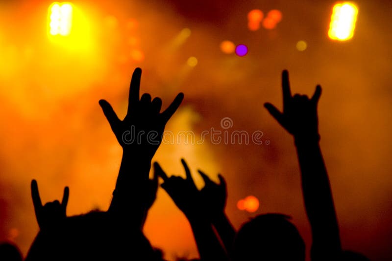 At a heavy metal concert the fans are showing the horn (sometimes called rock and roll) sign. The silhouettes of their hands are backed by colorful spotlights. At a heavy metal concert the fans are showing the horn (sometimes called rock and roll) sign. The silhouettes of their hands are backed by colorful spotlights.