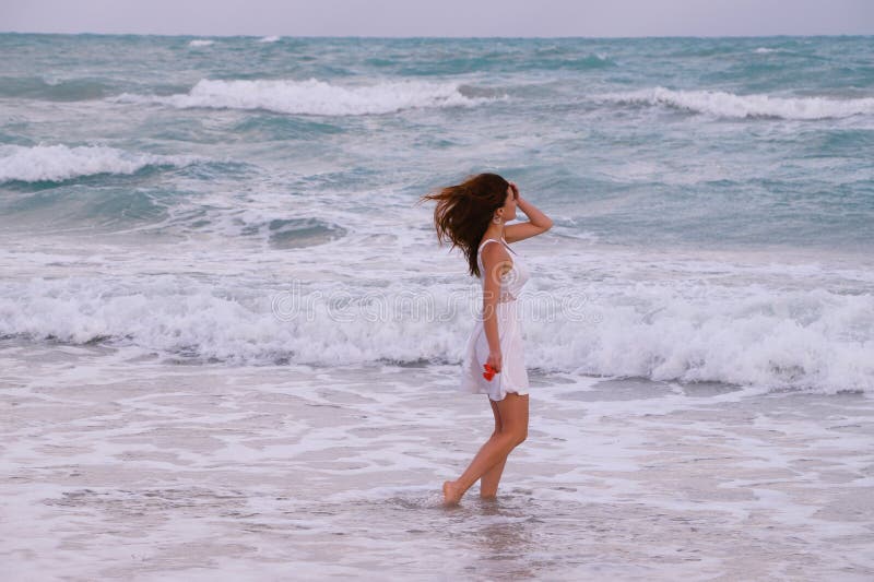 A slim, suntanned girl in a white dress walks the waves of the Caribbean Sea. A slim, suntanned girl in a white dress walks the waves of the Caribbean Sea