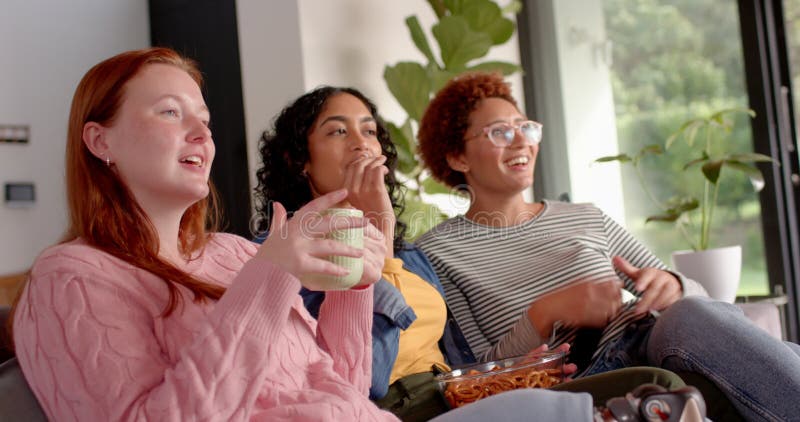 Ver televisión a varias amigas colgando en el sofá con aperitivos y bebidas almacen de video