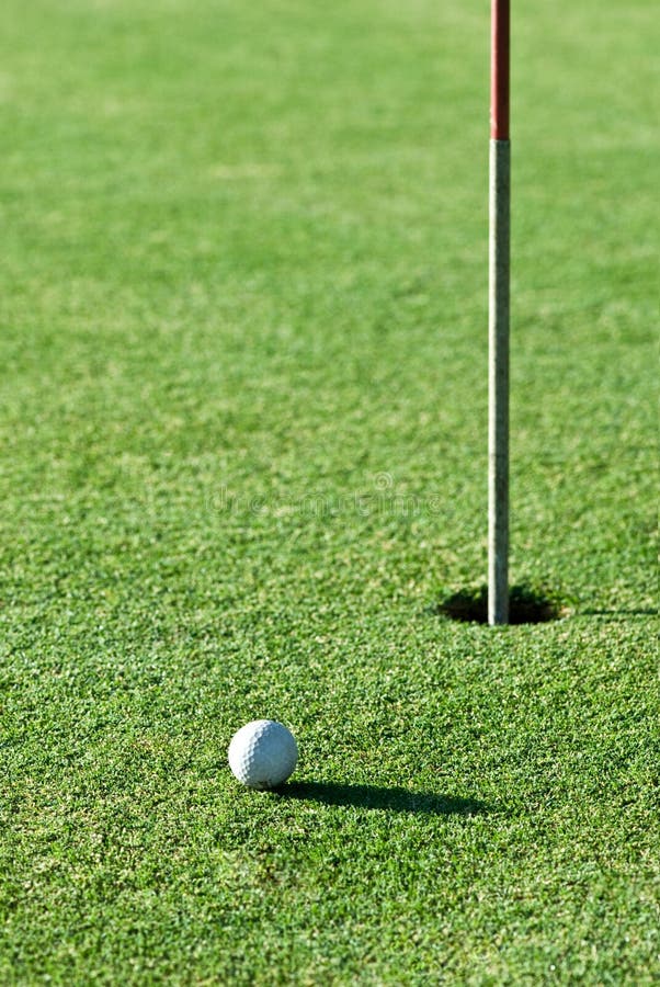 A golf ball a short putt away from the hole with the flag still in it. A golf ball a short putt away from the hole with the flag still in it.