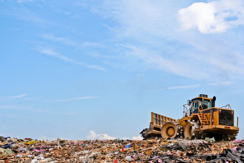 A compactor running at a landfill on top of a debris hill with a blue sky behind it. A compactor running at a landfill on top of a debris hill with a blue sky behind it.