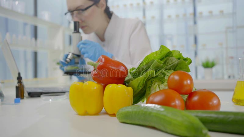 Verduras frescas em laboratório ao fundo de um cientista olhando pelo microscópio
