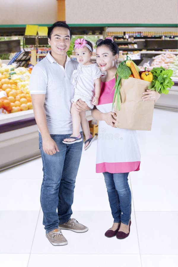 Full length of smiling family shopping vegetables while standing in supermarket. Full length of smiling family shopping vegetables while standing in supermarket