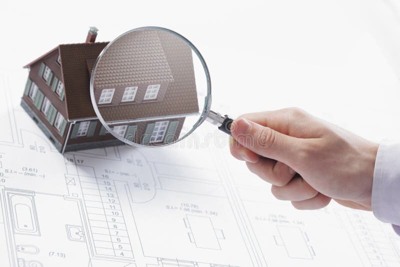 Concept image of a home inspection. A male hand holds a magnifying glass over a miniature house. Concept image of a home inspection. A male hand holds a magnifying glass over a miniature house.