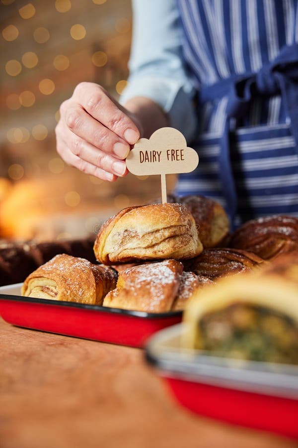 Verkaufsassistent in der Bäckerei setzen milchfreie Etikett in Stapel von frisch gebackenen Zimtbrötchen lizenzfreies stockfoto