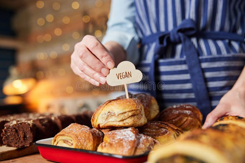Verkaufsassistent in der Bäckerei, der vegane Etiketten in frisch gebackene Zimtbrötchen steckt lizenzfreies stockfoto