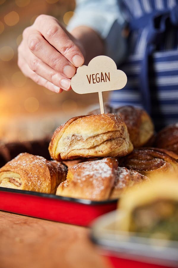 Verkaufsassistent in der Bäckerei, der vegane Etiketten in frisch gebackene Zimtbrötchen steckt lizenzfreies stockbild