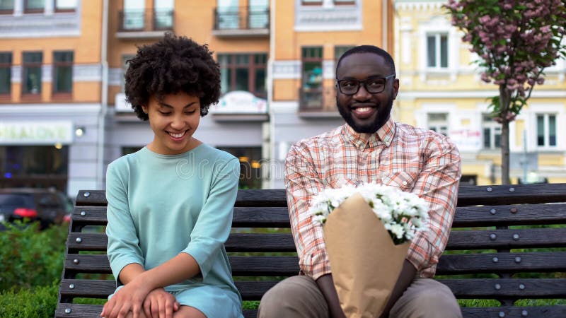 Verlegene Paare, die auf Bank mit Blumen, erstes Datum, Neigungsgefühle sitzen