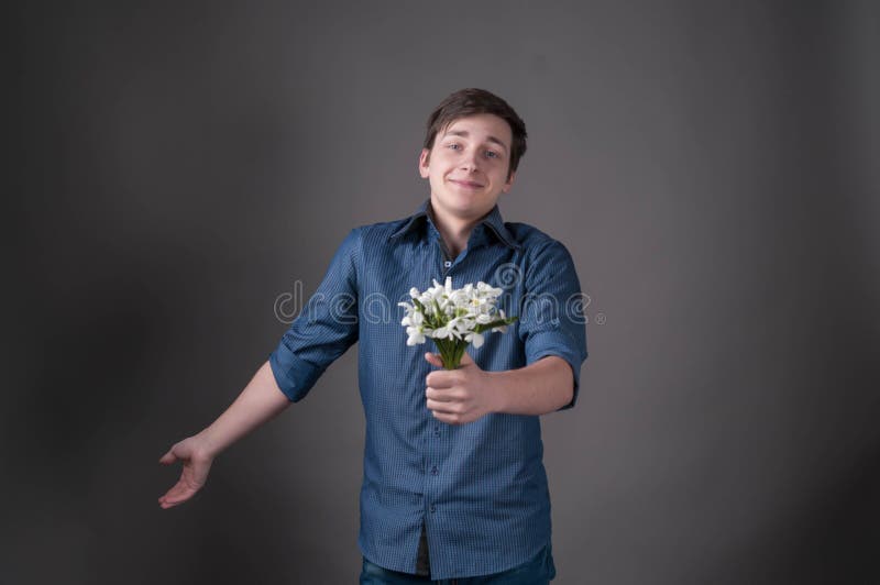 Verlegener junger Mann im blauen Hemdholdingblumenstrauß mit den Schneeglöckchen, Kamera und das Lächeln betrachtend lizenzfreies stockbild Verlegener junger Mann im blauen Hemdholdingblumenstrauß mit den Schneeglöckchen, Kamera und das Lächeln betrachtend lizenzfreies stockbild