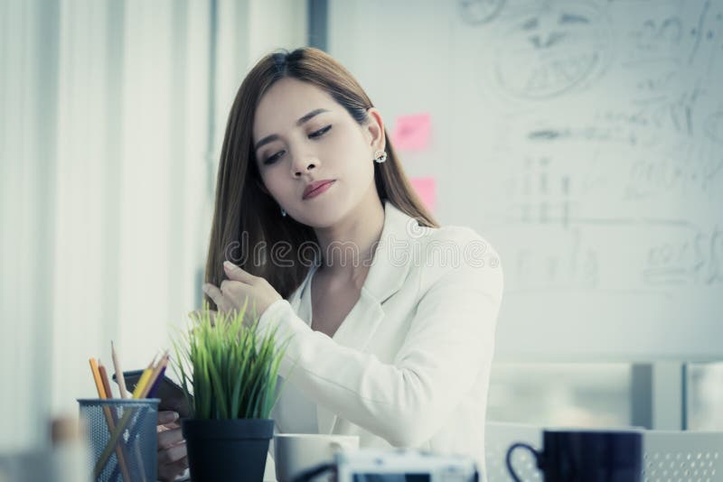Vermoeide bureauvrouw die mobiele telefoon met behulp van om haar schoonheid en haar te controleren royalty-vrije stock foto's Vermoeide bureauvrouw die mobiele telefoon met behulp van om haar schoonheid en haar te controleren royalty-vrije stock foto's