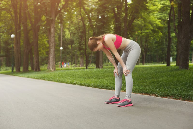 Tired runner breathing, taking run break in park. Athlete woman with hands on knees having rest after workout, copy space. Tired runner breathing, taking run break in park. Athlete woman with hands on knees having rest after workout, copy space