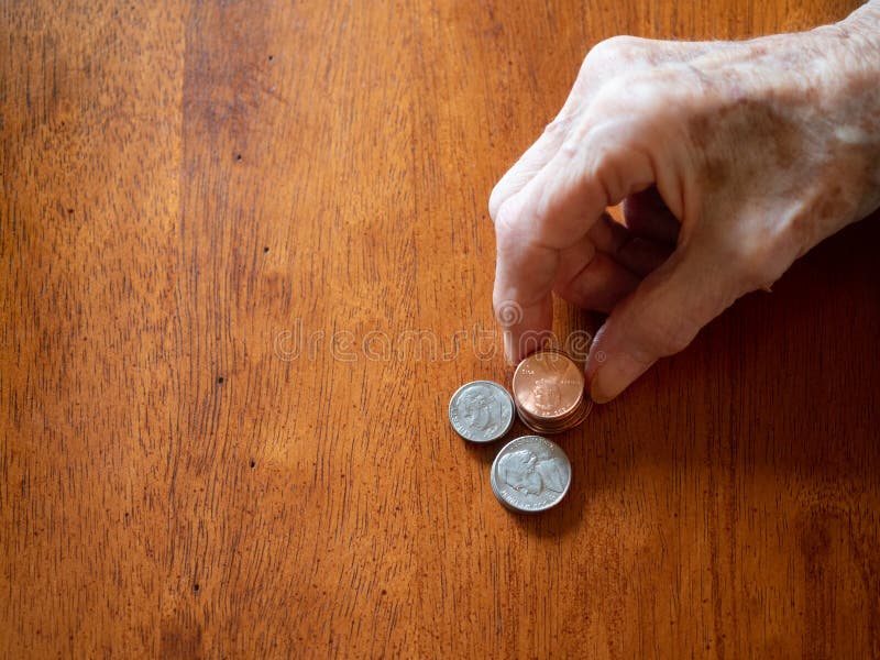 An elderly woman stacking pennies, nickles and dimes on a wooden table. Only her wrinkles hands are shown. Shallow depth of field. Copy space. An elderly woman stacking pennies, nickles and dimes on a wooden table. Only her wrinkles hands are shown. Shallow depth of field. Copy space