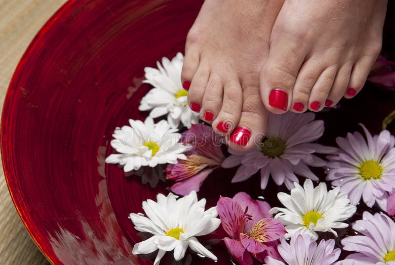 A women with red nail polish on her toes holds her feet above a bowl of water and flowers. A women with red nail polish on her toes holds her feet above a bowl of water and flowers.