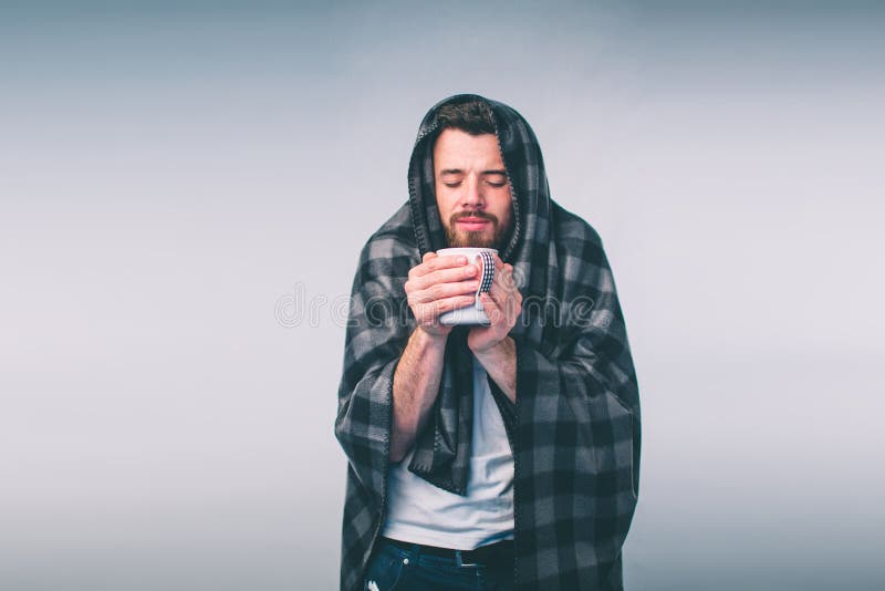 Verpakt in de warme deken of de plaid, zieke, jonge verwaande mens in glazen die warme het helen thee drinken stock afbeelding Verpakt in de warme deken of de plaid, zieke, jonge verwaande mens in glazen die warme het helen thee drinken stock afbeelding