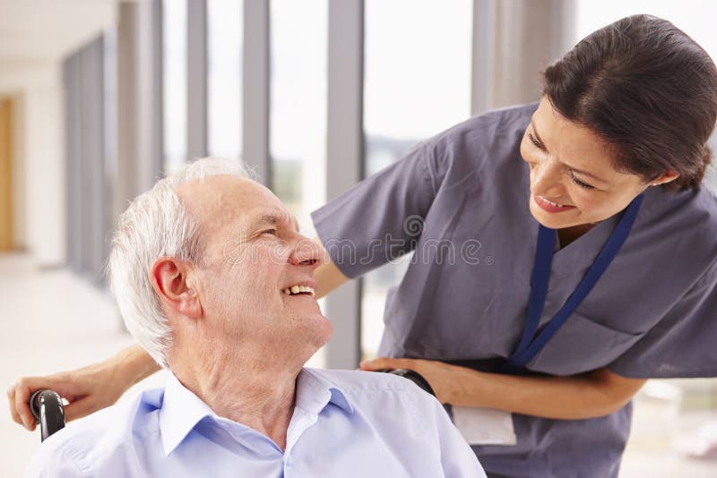 Nurse Pushing Senior Patient In Wheelchair Along Corridor. Nurse Pushing Senior Patient In Wheelchair Along Corridor