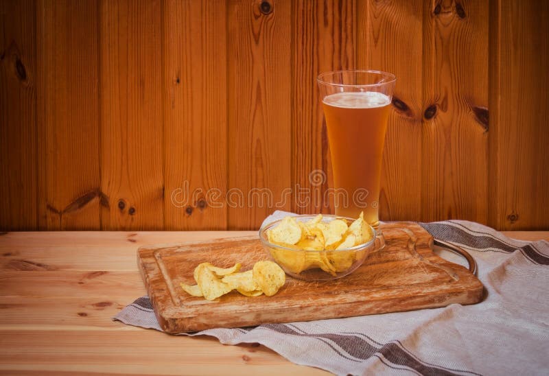 Verre de bière blonde avec des pommes chips sur la table en bois images libres de droits Verre de bière blonde avec des pommes chips sur la table en bois images libres de droits