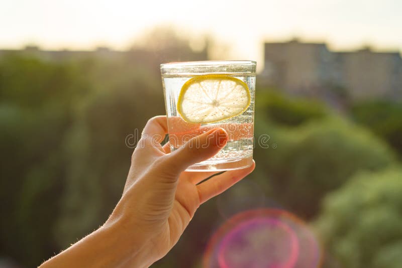 Verre de clair, l'eau de scintillement avec le citron à disposition Ciel de fond, silhouette de la ville, coucher du soleil photo stock Verre de clair, l'eau de scintillement avec le citron à disposition Ciel de fond, silhouette de la ville, coucher du soleil photo stock