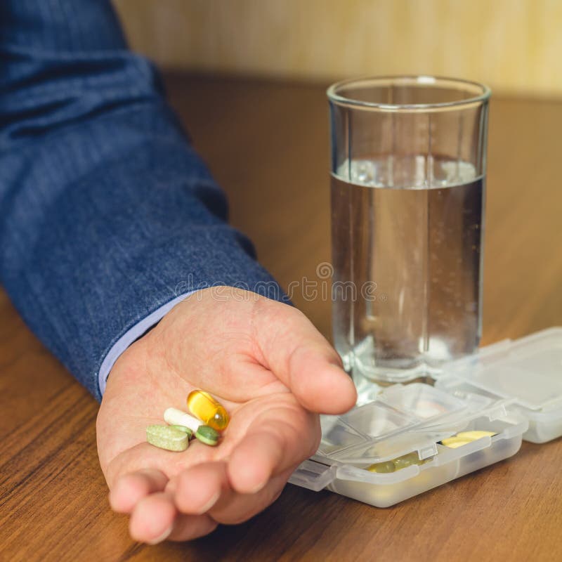 Verre de l'eau, de vitamines et de pilules de supplément nutritionnel et diététique se tenant à disposition de l'homme d'affaires image libre de droits Verre de l'eau, de vitamines et de pilules de supplément nutritionnel et diététique se tenant à disposition de l'homme d'affaires image libre de droits