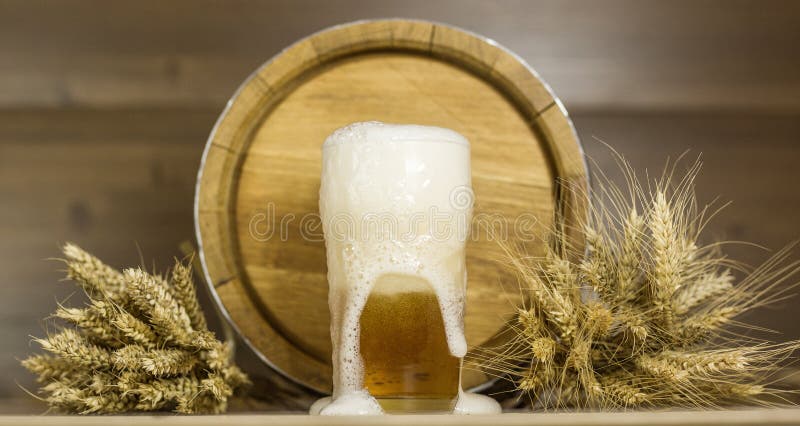 Verre et mousse de bière à l'arrière-plan du blé de barils image libre de droits Verre et mousse de bière à l'arrière-plan du blé de barils image libre de droits