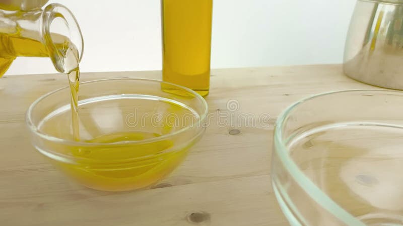 Versando cucinando olio d'oliva nell'imbottigliare il contenitore bianco sul fondo di legno della tavola vicino alla bottiglia di