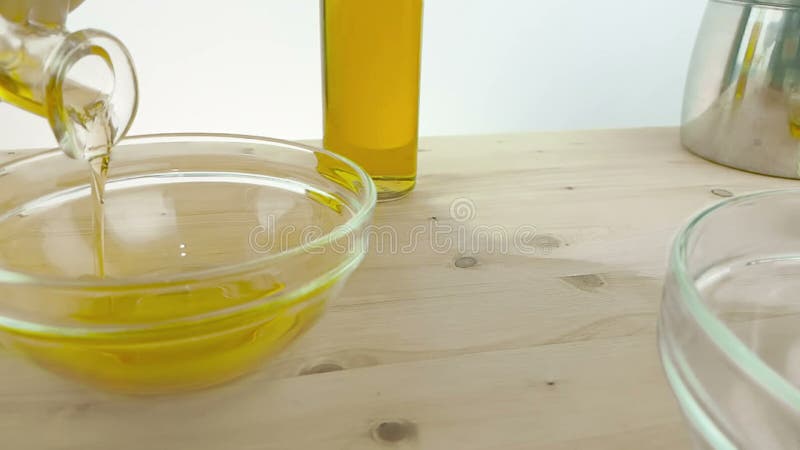 Versando cucinando olio d'oliva nell'imbottigliare il contenitore bianco sul fondo di legno della tavola vicino alla bottiglia di