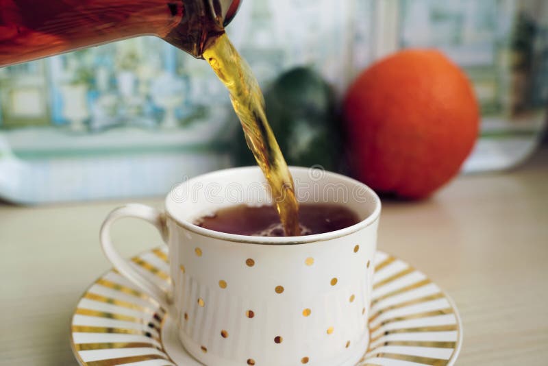 Versare tè aromatico in una tazza di teiera, i frutti sono sullo sfondo I mondiali e il piattino sono sul tavolo di legno della c fotografia stock libera da diritti Versare tè aromatico in una tazza di teiera, i frutti sono sullo sfondo I mondiali e il piattino sono sul tavolo di legno della c fotografia stock libera da diritti