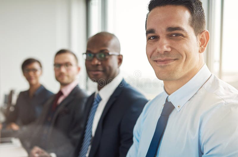 Diverse group of four grinning attractive business people sitting at table with back to large bright office window with light flare. Diverse group of four grinning attractive business people sitting at table with back to large bright office window with light flare