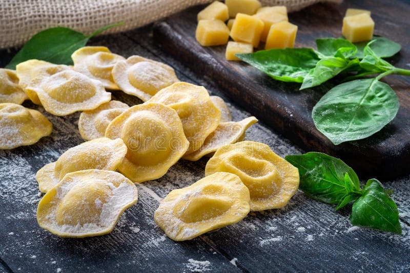 Fresh ravioli with cheese and Basil in flour on wooden background on kitchen table, dark background, close up. Fresh ravioli with cheese and Basil in flour on wooden background on kitchen table, dark background, close up