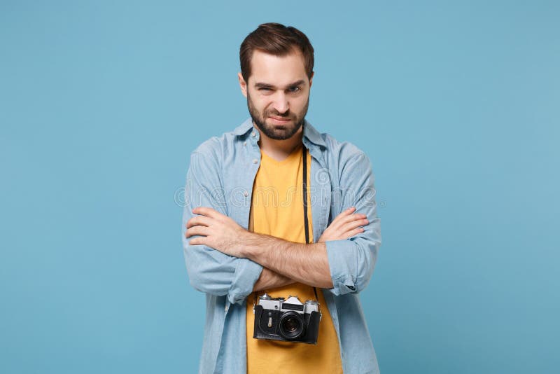 Displeased traveler tourist man in yellow summer clothes with photo camera isolated on blue background. Male passenger traveling abroad on weekends. Air flight journey concept. Holding hands crossed. Displeased traveler tourist man in yellow summer clothes with photo camera isolated on blue background. Male passenger traveling abroad on weekends. Air flight journey concept. Holding hands crossed