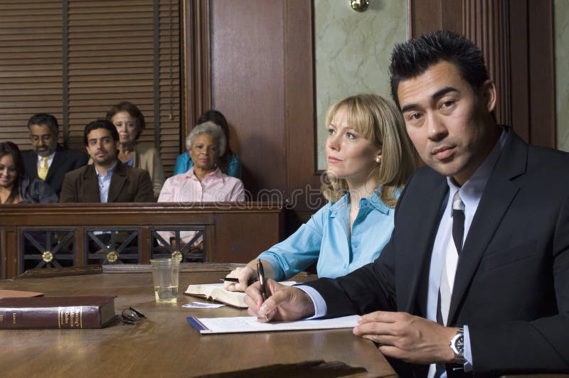 Portrait of a male defense lawyer sitting with client in courtroom. Portrait of a male defense lawyer sitting with client in courtroom