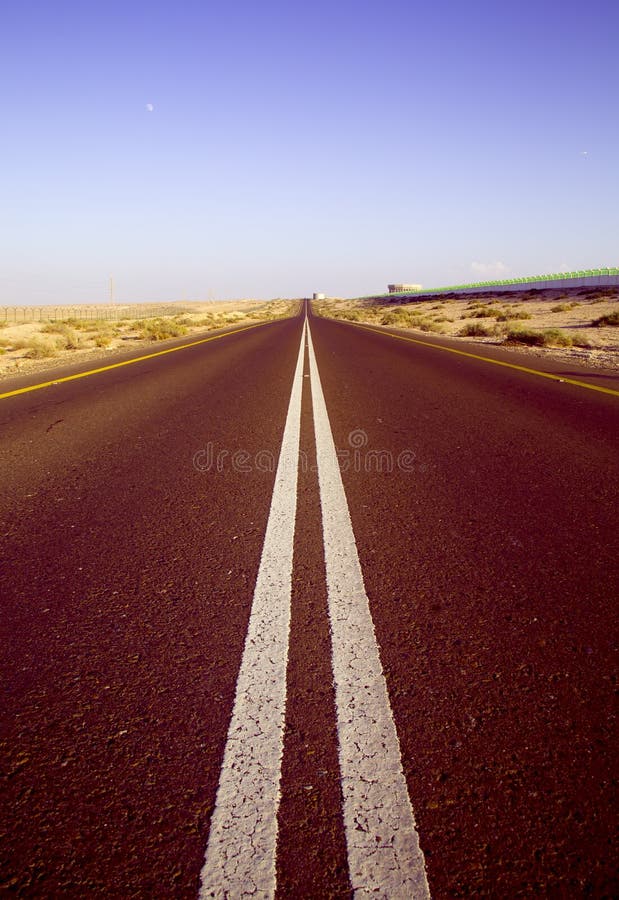 Verticaal schot van een rode, lege woestijnweg met rode tinten onder heldere blauwe hemel stock foto's Verticaal schot van een rode, lege woestijnweg met rode tinten onder heldere blauwe hemel stock foto's