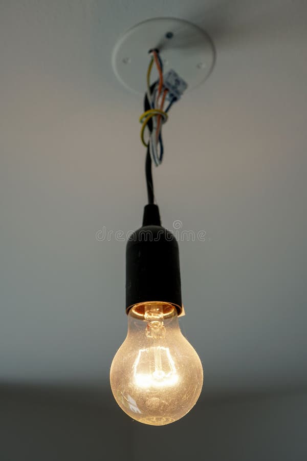 Vertical Closeup of a Light Bulb Hanging on a Ceiling at Home Stock