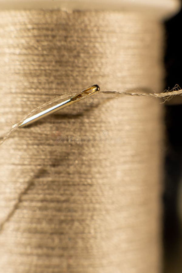 Vertical Closeup of a Needle with a Long Brown Thread Going through Its