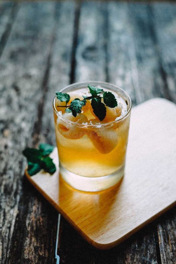 Vertical Closeup Shot Of An Alcoholic Cocktail In A Glass On Wooden Coaster With A Mint Leaf On Top