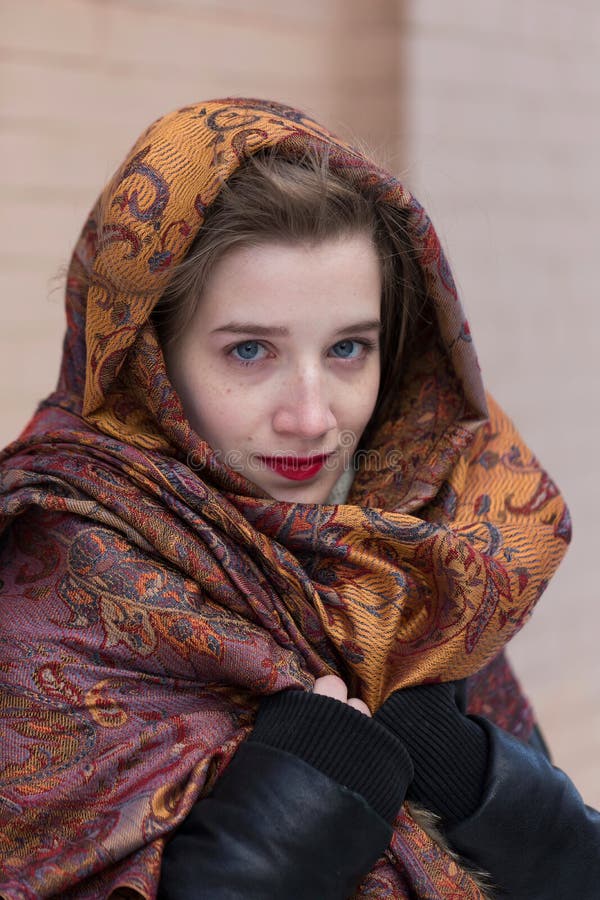 Young woman with blue eyes and red lipstick draping her head and shoulders in multicoloured shaw