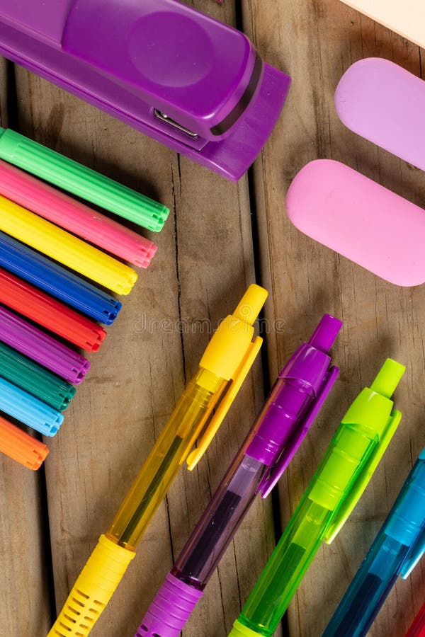 Vertical composition of colorful crayons, pens, markers and other school tools on wooden surface. School equipment, tools, learning and creativity concept.