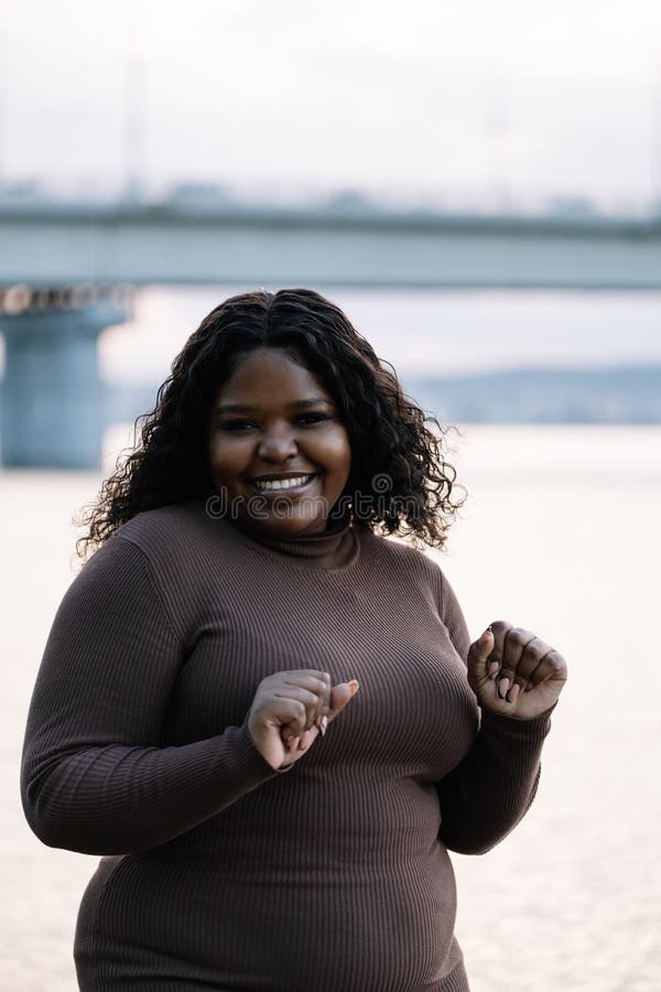 Vertical of cute smiling modern plump full figured interracialwoman near sea or river on summer vacation, look camera stock photography