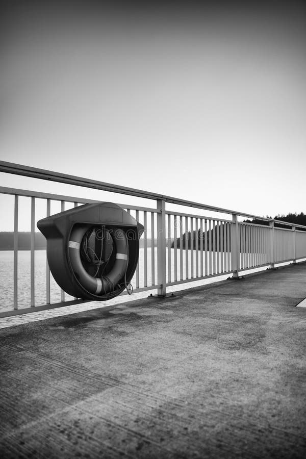 Vertical greyscale shot of a lifebuoy hanged on the iron railing of the bridge stock image